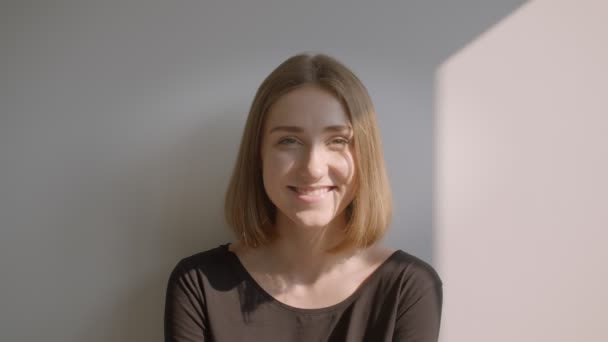 Rahat güneşli dairede evde mutlu bir şekilde gülümseyerek yerde oturan genç rahat beyaz beyaz kadın Closeup portre — Stok video