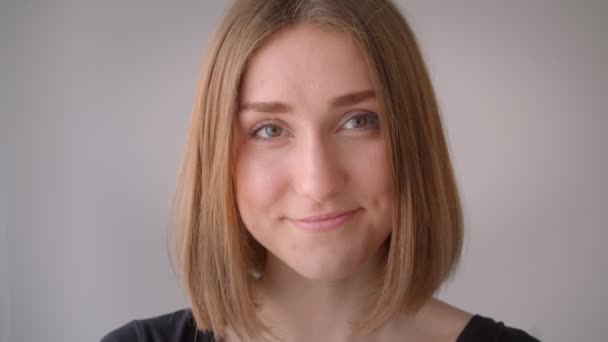 Portrét mladé, roztomile bělošské dívky s úsměvem na kameře v prázdném pokoji — Stock video