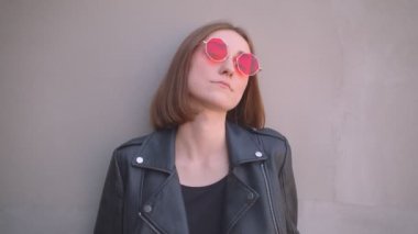 Kentsel şehirde açık havada kamera önünde poz bir deri ceket ve kırmızı güneş gözlüğü genç serin kafkas kız Closeup portre