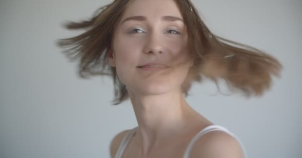 Primer plano de la joven hembra bastante caucásica con anillos de pelo y maquillaje brillo sonriendo felizmente girando a la cámara en la habitación blanca en el interior — Vídeos de Stock