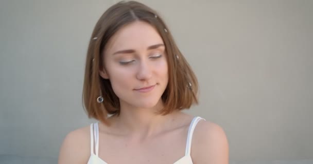 Nahaufnahme einer jungen hübschen kaukasischen Frau mit Haarringen und glitzerndem Make-up, die freudig in die Kamera im weißen Raum drinnen blickt — Stockvideo