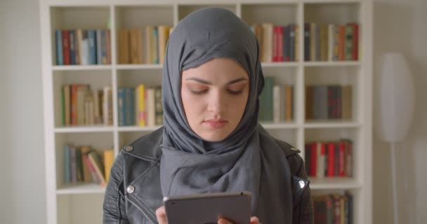 Retrato de primer plano de una joven atractiva estudiante musulmana en hijab usando la tableta mirando la cámara de la biblioteca universitaria en el interior — Vídeo de stock