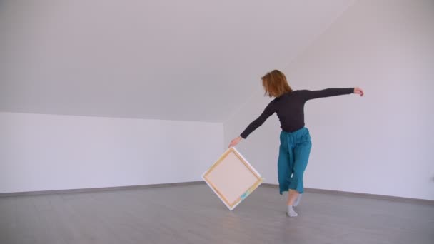 Motion shoot of young beautiful talented female performing an emotional dance with a picture in the empty room indoors in a flat — Stock Video