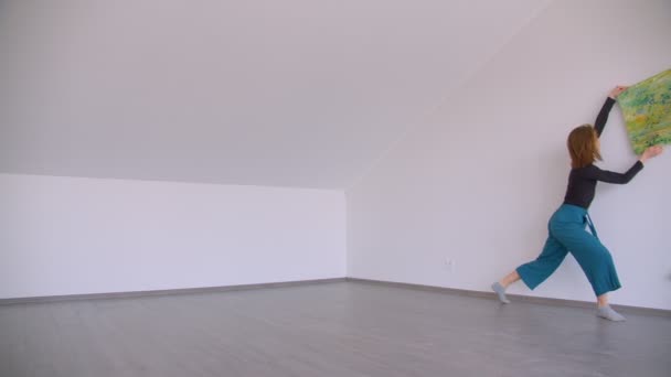 Motion shoot of young beautiful talented female performing an emotional dance with a picture leaning on the wall in the empty room indoors in a flat — Stock Video
