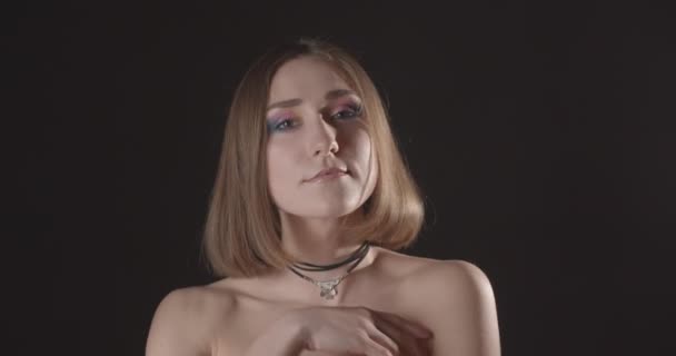 Nahaufnahme Shooting von jungen hübschen kaukasischen kurzhaarige Frau mit niedlichen Make-up und nackten Schultern Blick auf Kamera mit Hintergrund isoliert auf schwarz mit Schlaglicht — Stockvideo