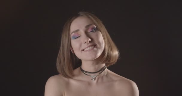 Střelili si mladou, krásnou, krátkovlasou ženskou s roztomilým make-upem s radostí s pohledem na kameru s pozadím na černém pozadí se světlým světlem — Stock video