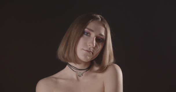 Close-up tiro de jovem muito caucasiano de cabelos curtos fêmea com maquiagem bonito olhando para a câmera com fundo isolado em preto com luz de clarão — Vídeo de Stock