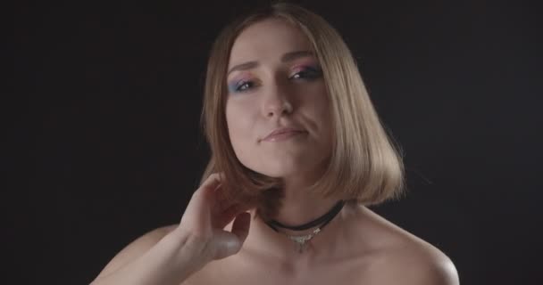 Zbliżenie strzelać młodego całkiem kaukaski krótkie włosy kobiece z cute makijaż uśmiechnięty uwodzicielsko patrząc na kamerę z tła na białym tle na czarno — Wideo stockowe