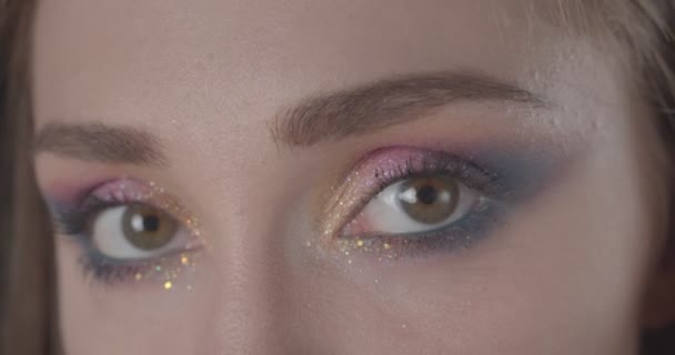 Close-up portret van jonge schattige Kaukasische kortharige vrouwelijk gezicht met glitter make-up kijken naar camera met achtergrond geïsoleerd op zwart — Stockvideo