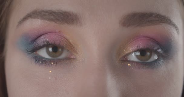 Close-up shoot van jonge mooie Kaukasische kortharige vrouwelijk gezicht met glitter make-up kijken naar camera met achtergrond geïsoleerd op zwart — Stockvideo