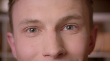 Üniversite kütüphanesinde kameraya bakan genç kendine güvenen beyaz erkek öğrencinin yakın çekim çekimi