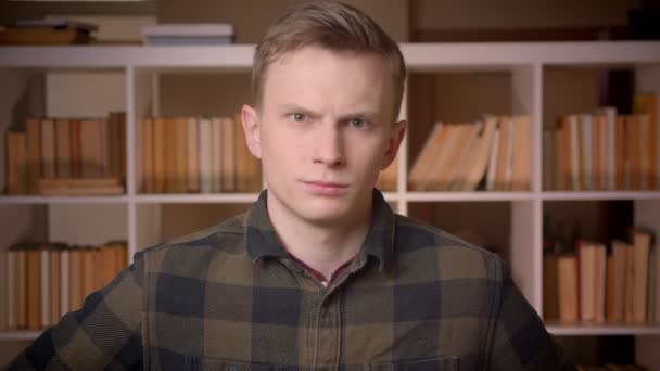 Closeup shoot of young attractive caucasian male student waving his head saying no being angry looking at camera in the college library — Stock Video