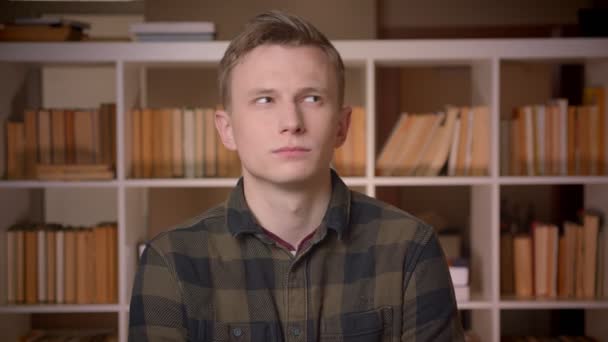 Närbild shoot av unga attraktiva kaukasiska manliga studenten dansa glatt framför kameran i kollegiet biblioteket — Stockvideo