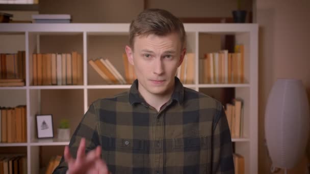 Крупним планом знімок молодого привабливого студента-чоловіка, який показує добре знак, дивлячись на камеру в бібліотеці коледжу — стокове відео