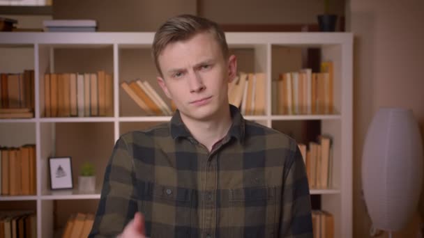 Closeup shoot of young attractive caucasian male student making a face palm being irritated and frustrated looking at camera in the college library — Stock Video