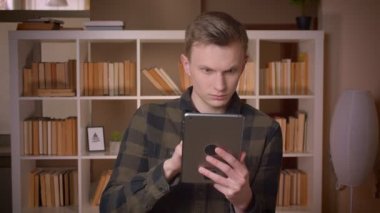 Üniversite kütüphanesinde tablette tarama genç çekici beyaz erkek öğrencinin closeup çekim