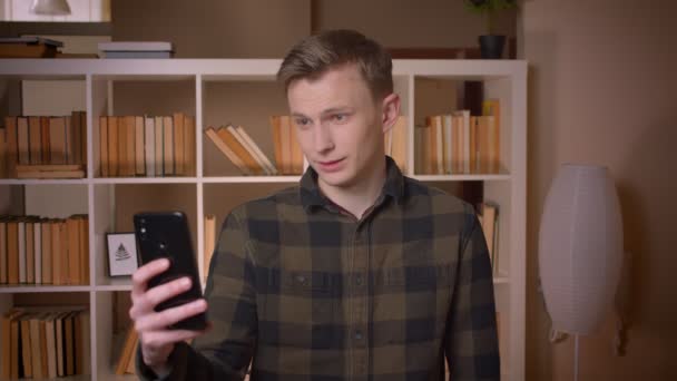 Närbild shoot av unga attraktiva kaukasiska manliga studenten tar selfies på telefonen i kollegiet biblioteket — Stockvideo