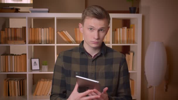 Gros plan shoot of young attractive caucasian male student using the tablet and showing blue chroma screen to camera in the college library — Video