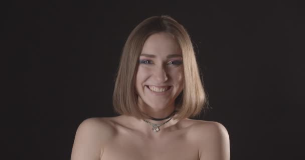 Close-up shoot van jonge mooie Kaukasische kortharige vrouw met leuke make-up glimlachend kijken naar camera met achtergrond geïsoleerd op zwart — Stockvideo