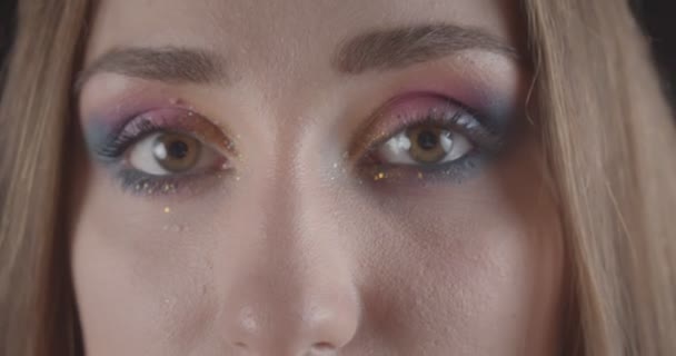 Zbliżenie portret młodego dość kaukaski krótkie włosy kobiece twarz z oczami z brokatem makijaż stwarzające przed kamerą z tła izolowane na czarno — Wideo stockowe