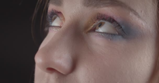 Gros plan portrait de jeune mignon caucasien à poils courts visage féminin avec les yeux avec un maquillage pailleté posant devant la caméra avec fond isolé sur noir — Video