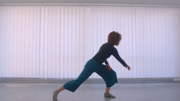 Bewegungsaufnahme einer jungen, ziemlich flexiblen Frau, die in einem leeren Raum in einer Wohnung einen emotionalen Tanz aufführt — Stockvideo