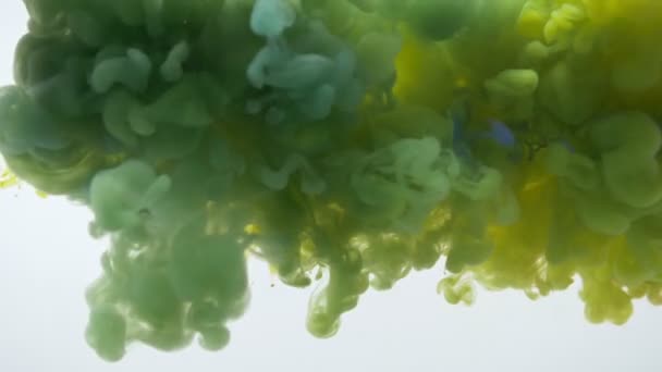 Close-up schieten van gele en blauwe aquarel inkt spatten en mengen veranderen in groen — Stockvideo