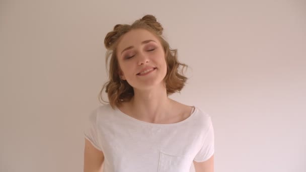 Närbild shoot av unga söta kaukasiska kvinna med hår bullar leende glatt tittar på kameran i vita rummet inomhus — Stockvideo