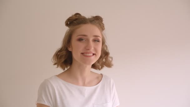 Съемки крупным планом молодой милой белой женщины с улыбкой на булочках и смехом, счастливо поворачивающейся к камере в белом помещении — стоковое видео