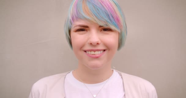 Крупним планом портрет молодої гіпсової білої жінки з пофарбованим волоссям, дивлячись на камеру на відкритому повітрі зі стіною на фоні — стокове відео
