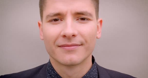 Nahaufnahme eines jungen, stylischen kaukasischen blonden Mannes, der glücklich in die Kamera lächelt, mit der Wand im Hintergrund — Stockvideo