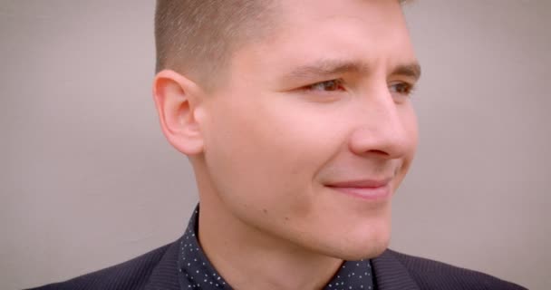 Closeup shoot of young stylish caucasian blonde man smiling cheerfully looking at camera with the wall on the background — Stock Video