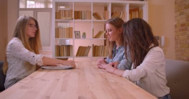 Genç güzel lezbiyen çift bir belge imzalayarak bir daire satın alma hakkında kadın emlakçı konuşurken closeup yan görünümü ateş ve kapalı masanın yanında oturan anahtarları alma