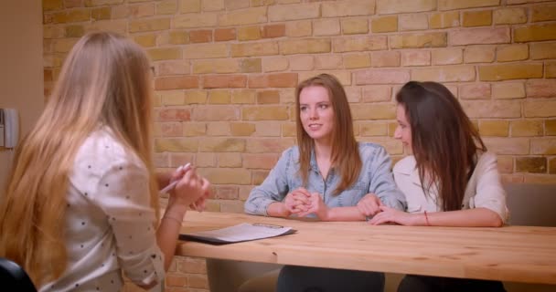 Närbild shoot av unga vackra lesbiska paret pratar med kvinnliga mäklaren om köp av en lägenhet som sitter vid bordet inomhus — Stockvideo