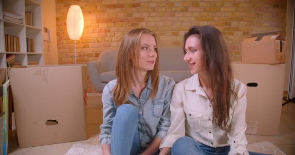 Closeup shoot of young beautiful lesbian couple bloggers talking on camera hugging and sitting on the floor in a newly bought apartment — Stock Video