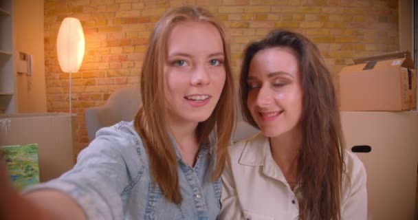 Closeup shoot of young beautiful lesbian couple bloggers talking on camera streaming live hugging and sitting on the floor in a newly bought apartment — Stock Video