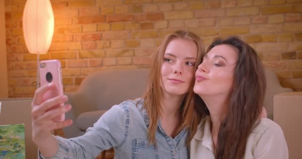 Closeup shoot of young beautiful lesbian couple taking selfies on the phone kissing and having fun sitting on the floor in a newly bought apartment — Stock Video