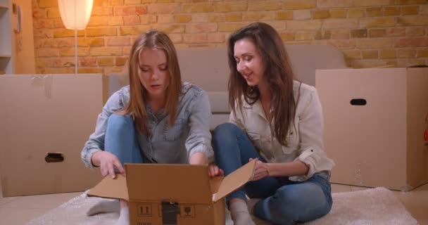 Closeup shoot of young beautiful lesbian couple unboxing and talking cheerfully sitting on the floor in a newly bought apartment — Stock Video