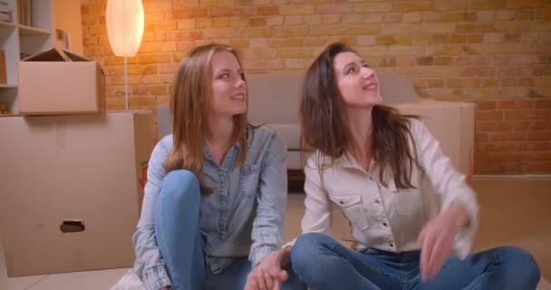 Closeup shoot of young beautiful lesbian couple holding hands and talking sitting on the floor in a newly bought apartment — Stock Video