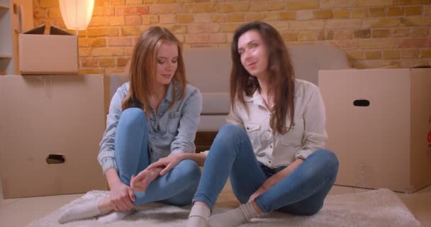 Съемки крупным планом молодых красивых лесбиянок, держащихся за руки, целующихся и разговаривающих, сидящих на полу в недавно купленной квартире — стоковое видео