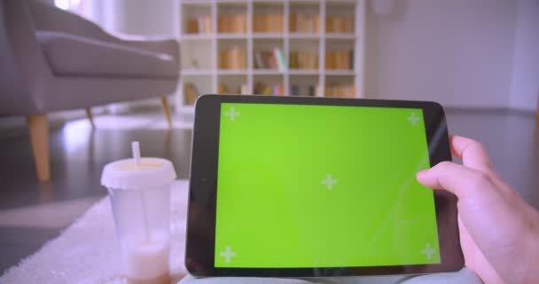 Manos caucásicas femeninas deslizando contenido en la pantalla de croma verde de la tableta en la sala de estar en los estantes de fondo . — Vídeo de stock