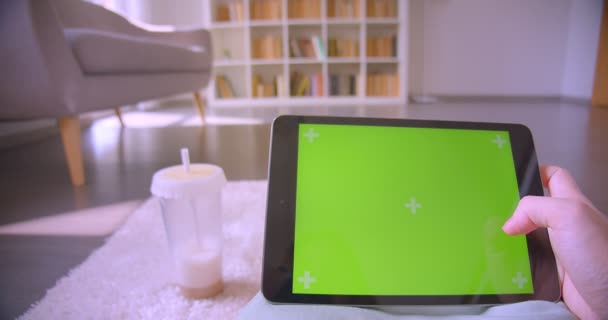 Manos caucásicas femeninas que trabajan en la pantalla de croma verde de la tableta en la sala de estar en los estantes de fondo . — Vídeos de Stock