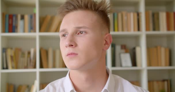 Closeup portrét mladého pohledného kavkazského studenta, který se dívá na kameru do univerzitní knihovny — Stock video