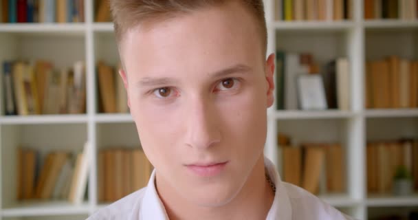 Üniversite kütüphanesinde kameraya mutlu bir şekilde bakan genç yakışıklı beyaz erkek öğrencinin yakın çekim portresi — Stok video
