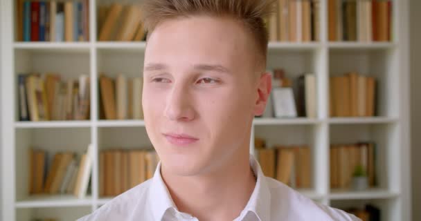 Closeup portréja fiatal magabiztos kaukázusi Férfi diák mosolygós vidáman nézi kamera a főiskola könyvtár — Stock videók