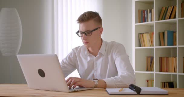 Primer plano retrato de joven guapo hombre de negocios caucásico en gafas usando el portátil en el interior de la oficina — Vídeos de Stock