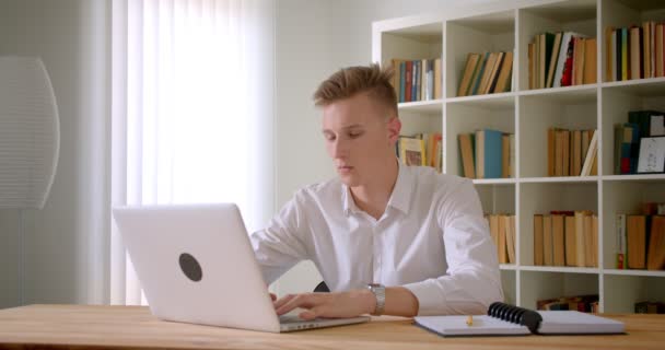 オフィスの屋内でラップトップを使用して若いハンサムな白人ビジネスマンのクローズアップ肖像画 — ストック動画