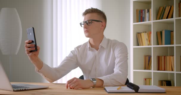 Zbliżenie portret młodego przystojnego kaukaski biznesmen w okularach robienia selfie na telefon pozowanie przed kamerą w pomieszczeniu w biurze — Wideo stockowe