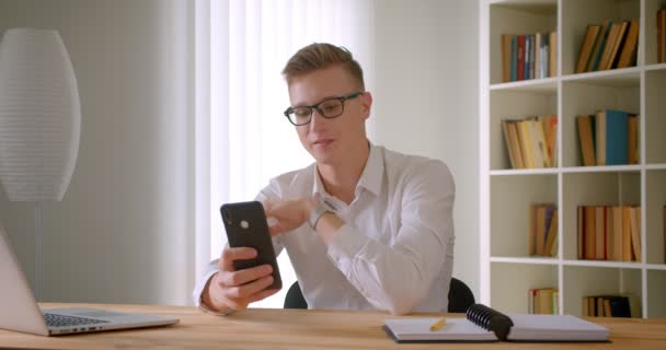 Zbliżenie portret młodego przystojnego kaukaski biznesmen w okularach robienia selfie na telefon uśmiechając się wesoło pokazując dwa palce w pomieszczeniu w biurze — Wideo stockowe