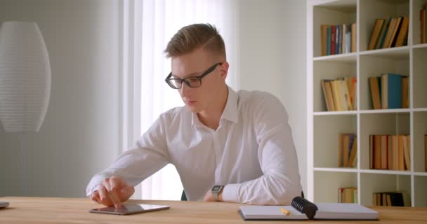 Primo piano ritratto di giovane uomo d'affari caucasico bello in bicchieri utilizzando la tavoletta all'interno dell'ufficio — Video Stock